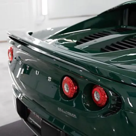 Rear view of dark green Lotus sports car showing taillights and spoiler in bright showroom.