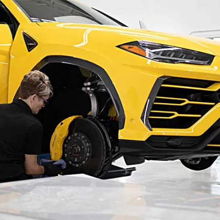 Technician working on the brake system of a lifted yellow luxury sports SUV in a clean garage.