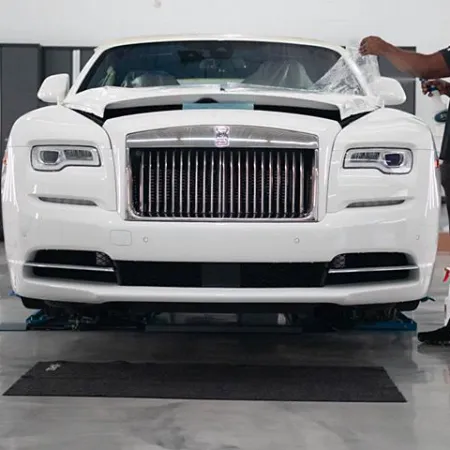 Man applying protective film on the hood of a white luxury Rolls-Royce car indoors.