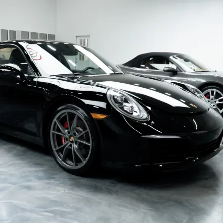 Black and gray Porsche sports cars parked inside a glossy showroom with concrete flooring and modern lighting.