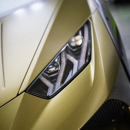 Close-up of a sleek gold sports car's angular headlight and aerodynamic front detailing.