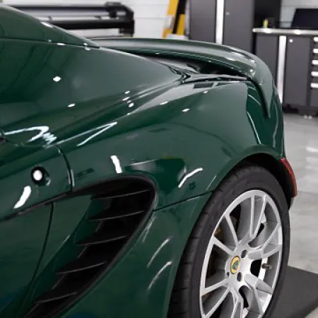 Close-up of a dark green sports car rear side showcasing wheel and aerodynamic body vents in a modern garage.