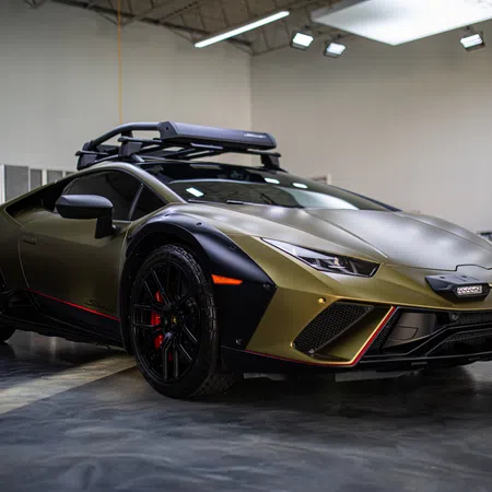 Matte gold and black sports car with roof rack inside a spacious garage under bright lighting.