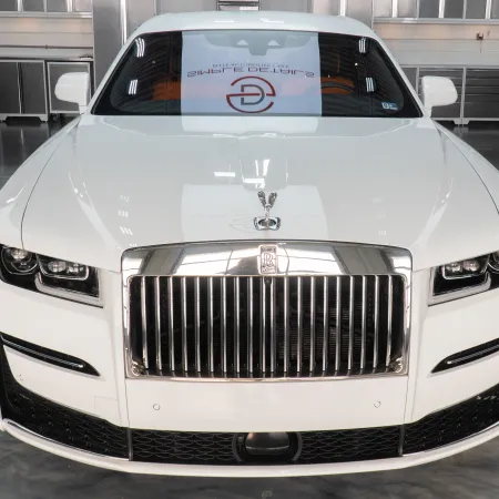 Front view of elegant white Rolls-Royce luxury car parked in modern showroom with polished floor.