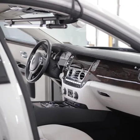 Luxury car interior with black steering wheel, wood panel dashboard, white seats, and modern controls visible.