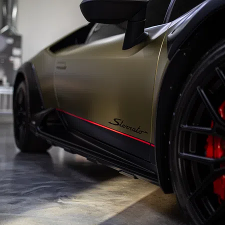 Close-up of a matte gold luxury sports car side with red accents and black wheel with red brake calipers.
