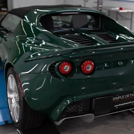 Dark green Lotus sports car rear view with round taillights parked indoors on a lift.