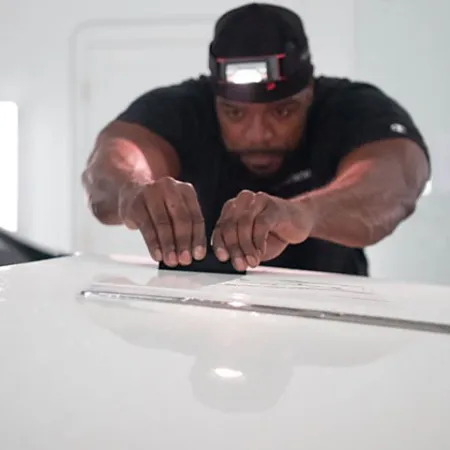 Man wearing headlamp carefully sanding the roof of a white car in a workshop for detailing.