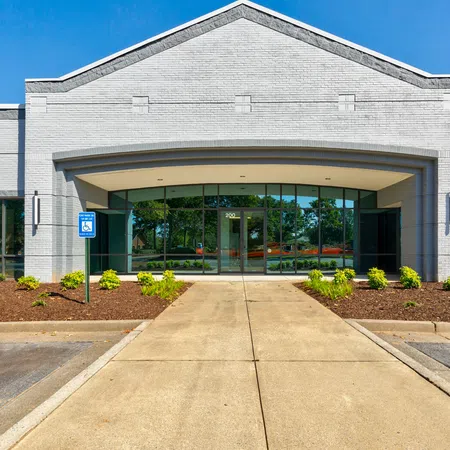 Modern commercial building entrance with glass doors, landscaped garden, and blue sky in background
