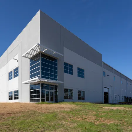 Modern industrial warehouse building with large windows and loading docks under clear blue sky.