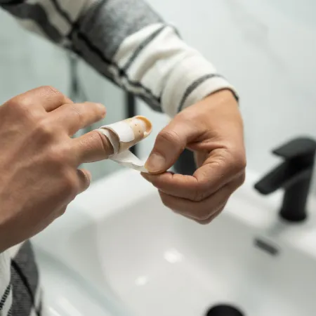 Person wrapping a bandage around a cut finger over a white sink with a black faucet