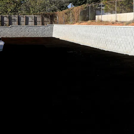 White car parked beside a newly built concrete retaining wall under bright sunlight near a wooden fence.