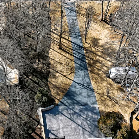 Aerial view of a curved driveway with long tree shadows on dry grass and leafless trees around homes.