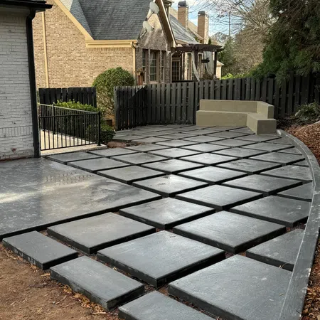 Modern backyard patio with geometric concrete pavers and built-in corner seating surrounded by a black fence.
