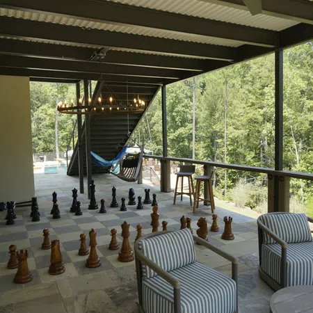 Covered outdoor patio with giant chess set, striped armchairs, hammock, bar stools, and forest view