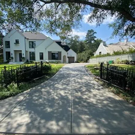 Long driveway leading to a modern white house with black trim, surrounded by green trees and a sunny sky.