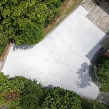 Aerial view of a large, empty white concrete driveway surrounded by green trees and shrubs.