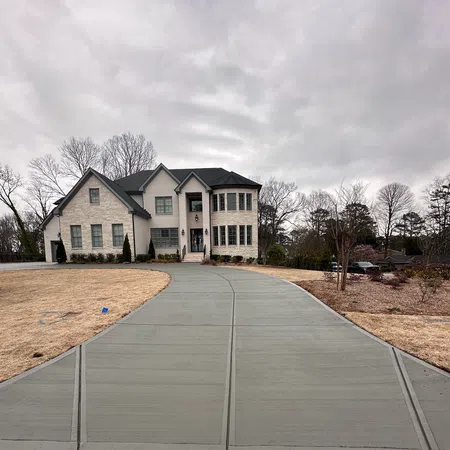 Large two-story house with beige brick exterior and wide concrete driveway under cloudy sky.