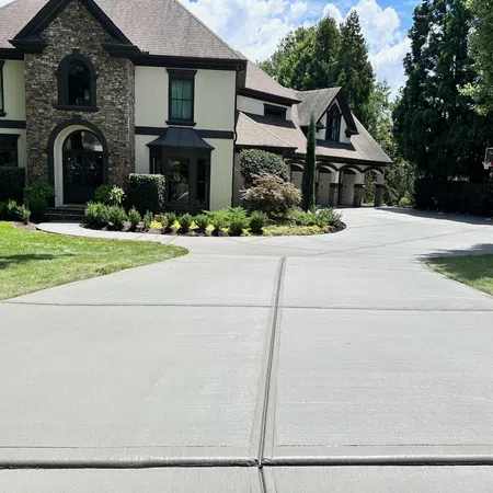 Modern two-story house with stone and cream exterior and wide concrete driveway under a partly cloudy sky.