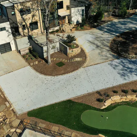 Aerial view of modern house with large driveway, landscaped garden, and a small golf putting green.