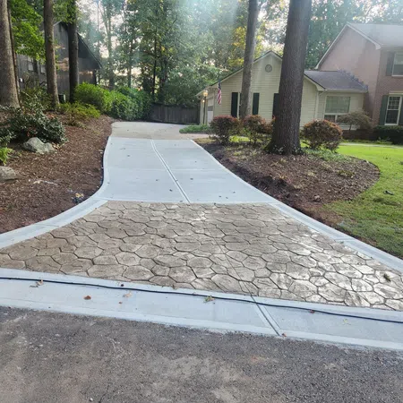 Newly poured driveway with stamped concrete in front of a suburban home surrounded by trees and garden beds.