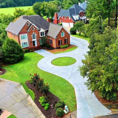 Aerial view of large red brick suburban houses with curved concrete driveways and lush green lawns.