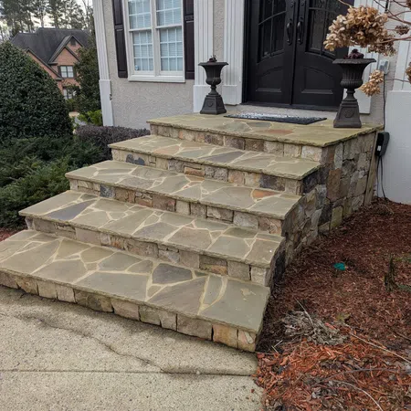 Natural stone flagstone treads with a stacked stone veneer raise leading to a black double door entrance with decorative urns and adjacent garden beds.