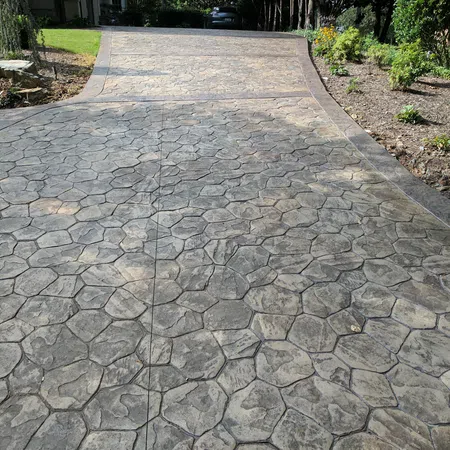Stamped concrete driveway with hexagonal stone pattern leading up to a garage surrounded by greenery and landscaping
