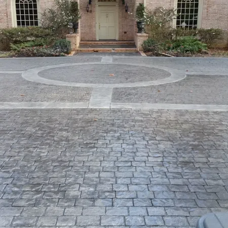 Stamped concrete driveway with a circular pattern leading to a brick house entrance with greenery