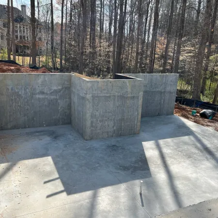 Concrete foundation walls for a new residential house under construction surrounded by trees and soil.