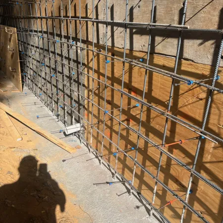 Metal rebar grid attached to wooden formwork for concrete wall construction at sunny building site.