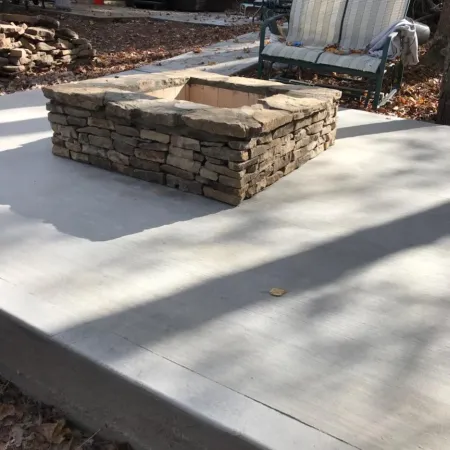 A stone fire pit on a concrete patio surrounded by autumn leaves and a garden chair.