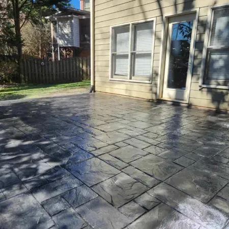 Stylish stamped concrete patio with a sleek gray finish beside a home, featuring sunlight and shadows.