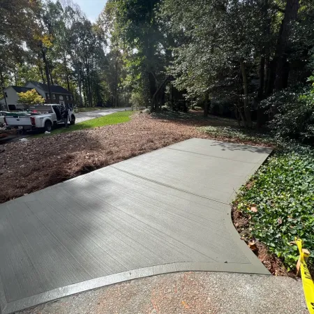 Freshly poured concrete walkway surrounded by trees and greenery on a sunny day.