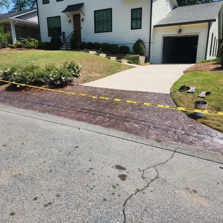 Newly stamped concrete driveway entrance with caution tape in front of a modern white house with garden.