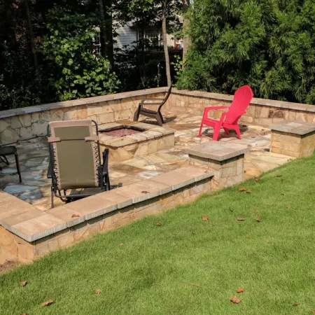 A cozy stone fire pit area surrounded by green grass and colorful lounge chairs for outdoor gatherings.