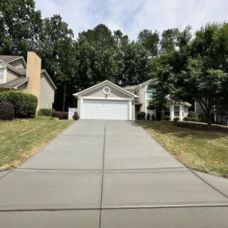 Freshly poured concrete driveway leading to a two-car garage with surrounding green lawn and trees.