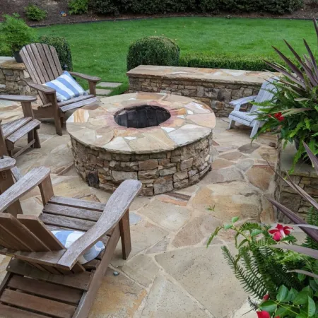 Cozy outdoor fire pit surrounded by wooden chairs and lush greenery in a serene backyard setting.
