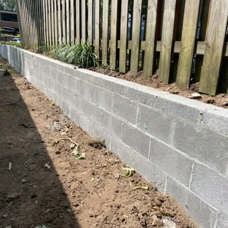 Newly built gray cinder block retaining wall supporting wooden fence with garden bed on top
