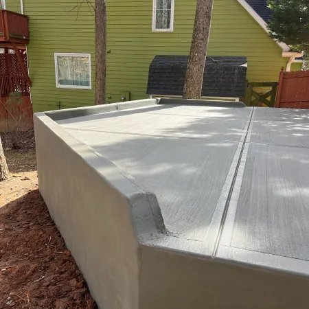 Newly poured smooth concrete slab foundation near a green house and red wooden structure in a backyard.