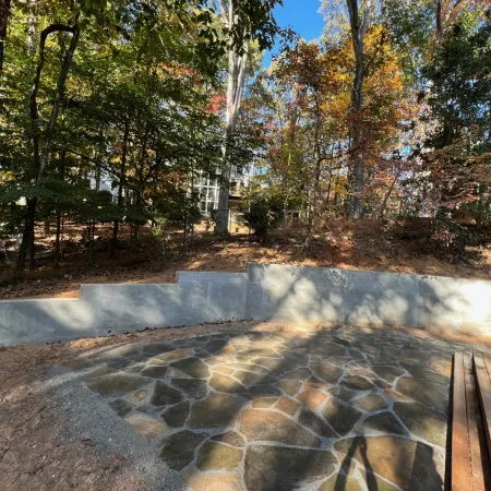 Stone patio surrounded by a low concrete wall and autumn trees under a clear blue sky in a backyard.
