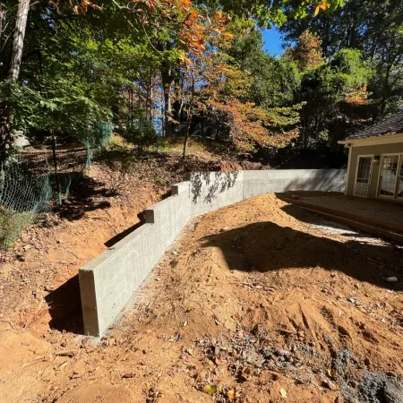 Newly constructed concrete retaining wall along a sloped yard beside a house with autumn trees.