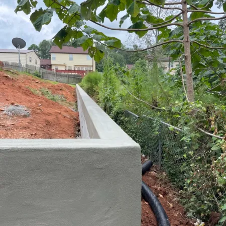 a concrete wall with a fence and trees and a building in the background