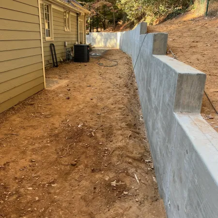 Newly constructed concrete retaining wall next to a house with exposed dirt ground and fall trees in background