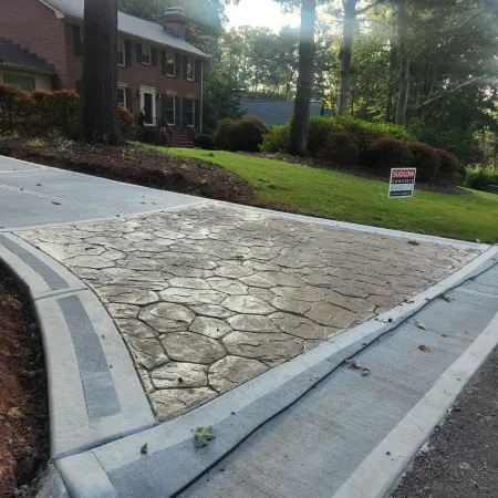 Stamped concrete driveway with a textured pattern in front of a brick house and green lawn.