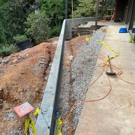 New concrete retaining wall construction next to gravel and a patio with tools and caution tape visible