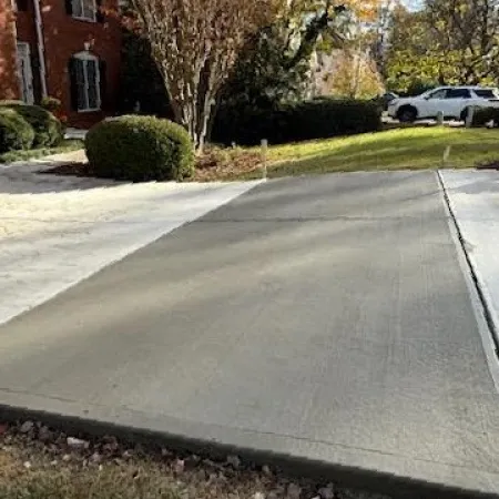 Freshly poured concrete driveway blending with existing paved surfaces, surrounded by landscaped yard.