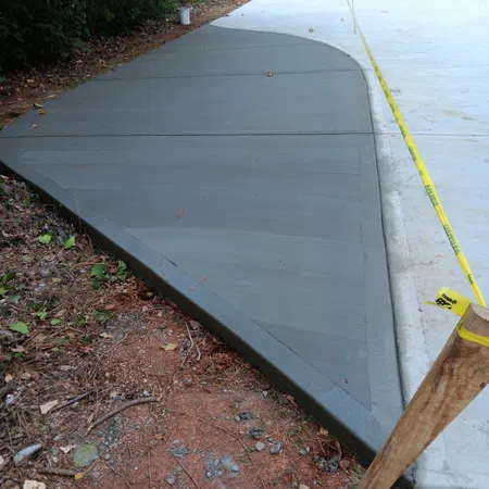 Freshly poured concrete driveway with wet and dry sections cordoned off by caution tape and wooden stakes.