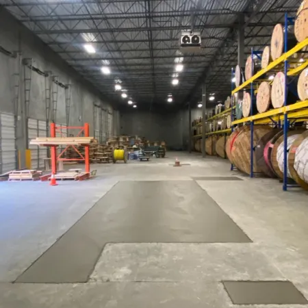 Spacious warehouse interior showcasing large rolls of material and a concrete floor under bright lighting.