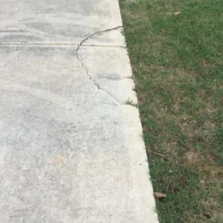 Cracked concrete driveway with green grass nearby, highlighting surface damage and lawn contrast.